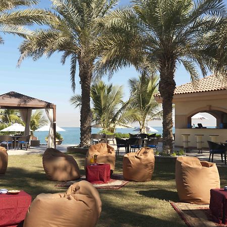 Al Raha Beach Resort & Spa Abu Dhabi Restaurante foto The photo depicts a beautiful outdoor setting with several elements of relaxation and leisure. In the foreground, there are large, comfortable bean bag chairs arranged on a grassy area, accompanied by low tables. Surrounding this seating area are tal