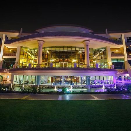 Al Raha Beach Resort & Spa Abu Dhabi Exterior foto The photo shows a modern architectural building illuminated at night. The structure has a large central entrance with multiple glass windows, flanked by symmetrical columns. The exterior features a combination of sleek lines and curves, with lighting