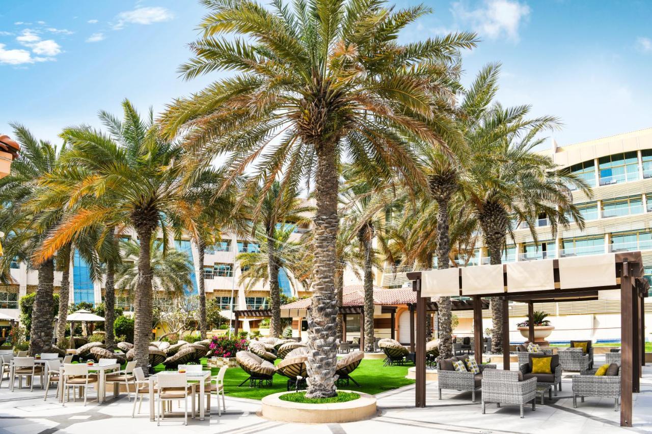 Al Raha Beach Resort & Spa Abu Dhabi Exterior foto The photo shows a picturesque outdoor area, likely at a resort or hotel. It features several tall palm trees that provide a tropical feel. In the foreground, there are several lounge chairs and seating arrangements, suggesting a relaxing environment.