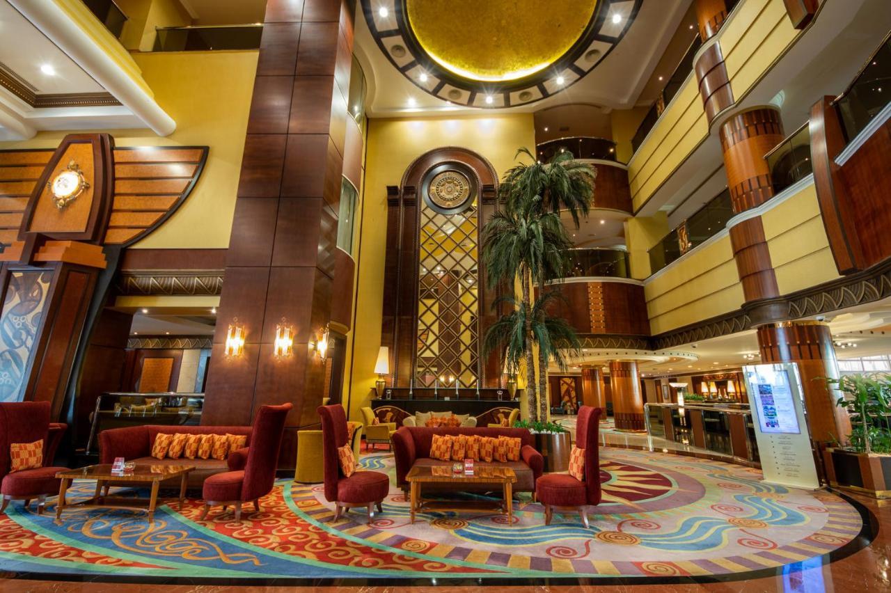 Al Raha Beach Resort & Spa Abu Dhabi Exterior foto The photo shows an elegant lobby interior of a hotel. The space features tall ceilings with decorative lighting and large windows, allowing for natural light. There are several plush seating arrangements, including red armchairs and wooden tables, cr