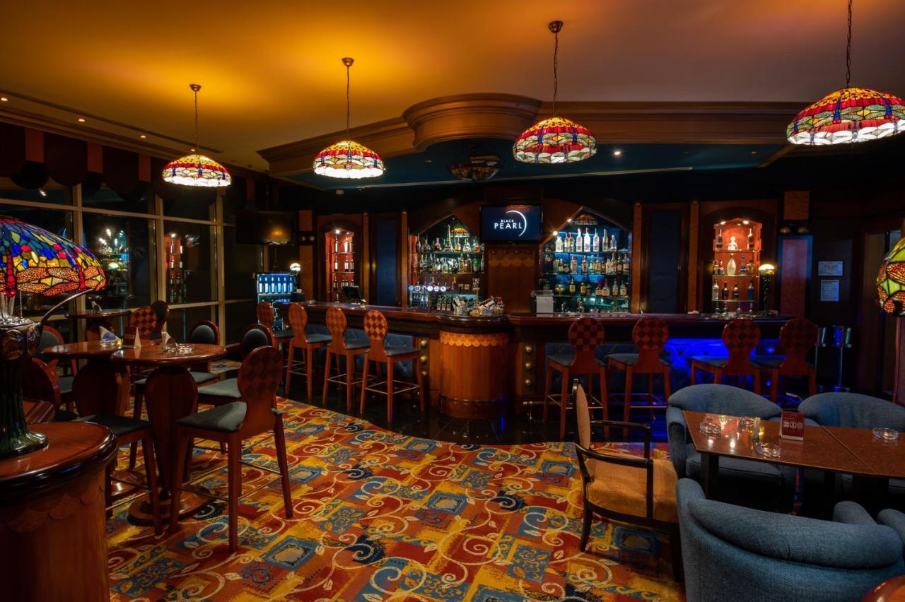 Al Raha Beach Resort & Spa Abu Dhabi Exterior foto The photo shows a cozy bar interior, featuring a well-stocked bar area with various bottles displayed on shelves. The bar is illuminated by colorful stained glass light fixtures, creating a warm and inviting atmosphere. The floor is covered with a vi
