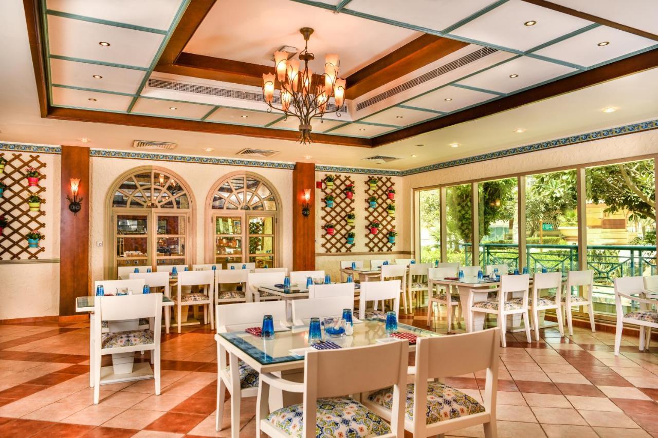 Al Raha Beach Resort & Spa Abu Dhabi Exterior foto The photo shows the interior of a restaurant or dining area. The space has a warm and inviting atmosphere, featuring a mix of decorative elements. 

- **Seating**: There are several white wooden tables and chairs arranged throughout the area, some wi