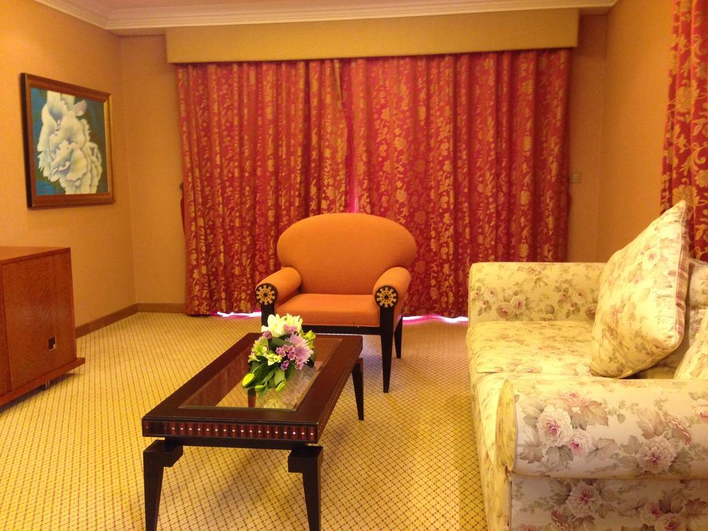 Al Raha Beach Resort & Spa Abu Dhabi Exterior foto The photo shows a cozy living room setting. There is an orange chair with decorative armrests situated near a floral-patterned sofa. A coffee table with a floral arrangement sits in front of the sofa. The room is adorned with warm colors, complementi