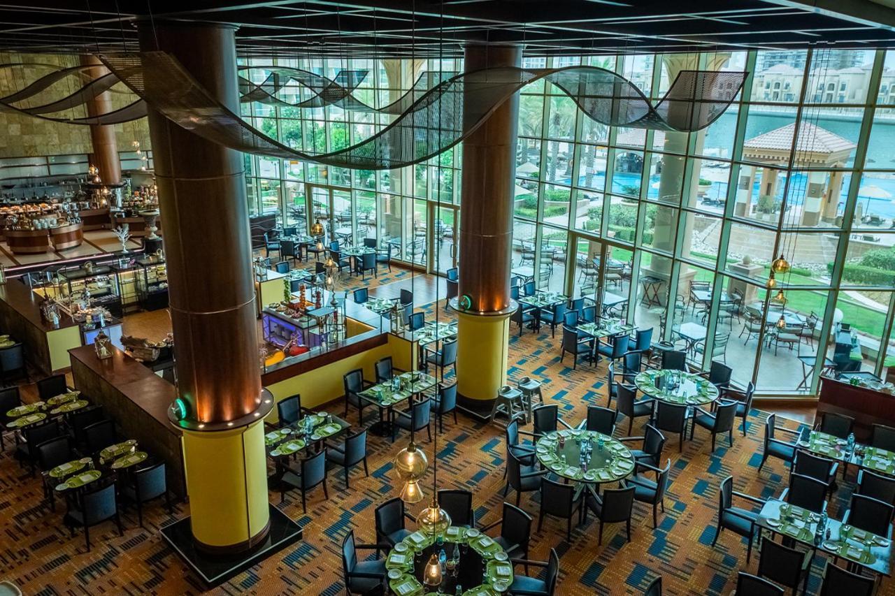 Al Raha Beach Resort & Spa Abu Dhabi Exterior foto The photo shows the interior of a restaurant with a modern design. It features large windows allowing natural light to flood the space, creating an inviting atmosphere. The dining area is furnished with round tables covered with green tablecloths and