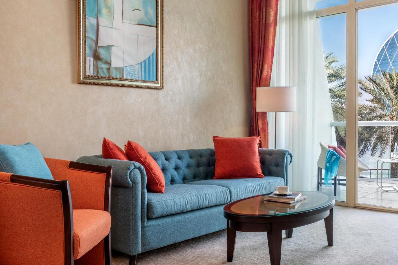 Al Raha Beach Resort & Spa Abu Dhabi Exterior foto The photo shows a well-decorated living room. There is a plush blue couch with orange accent pillows and a cozy orange armchair nearby. A round coffee table sits in front of the couch, and above it, there is a colorful painting hanging on the wall. L