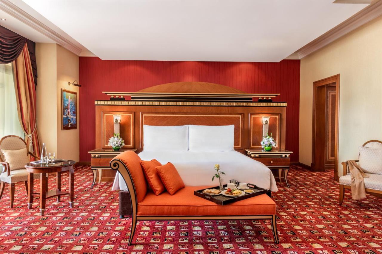 Al Raha Beach Resort & Spa Abu Dhabi Exterior foto The photo shows an elegantly designed hotel room. The room features a large bed with white linens and a decorative headboard. The walls are painted in a warm red color, and there are side tables with lamps beside the bed. 

There is an orange sofa or