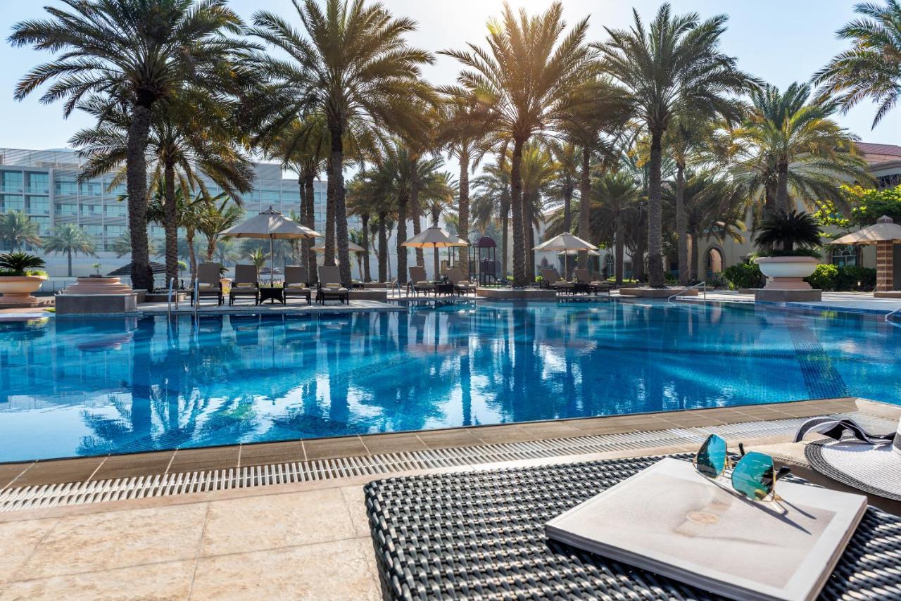 Al Raha Beach Resort & Spa Abu Dhabi Exterior foto The photo shows a vibrant swimming pool surrounded by palm trees under a clear sky. The pool's water is sparkling in the sunlight, creating a serene and inviting atmosphere. Lounge chairs are placed around the pool, some of which are shaded by umbrel
