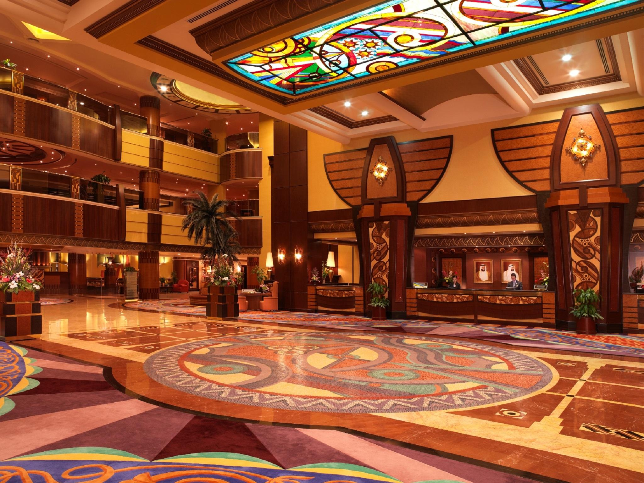 Al Raha Beach Resort & Spa Abu Dhabi Interior foto The photo depicts an elegantly designed hotel lobby. It features a grand ceiling with intricate stained glass and decorative patterns. The floor is adorned with colorful, ornate designs, including circular patterns. The lobby is spacious, with wooden