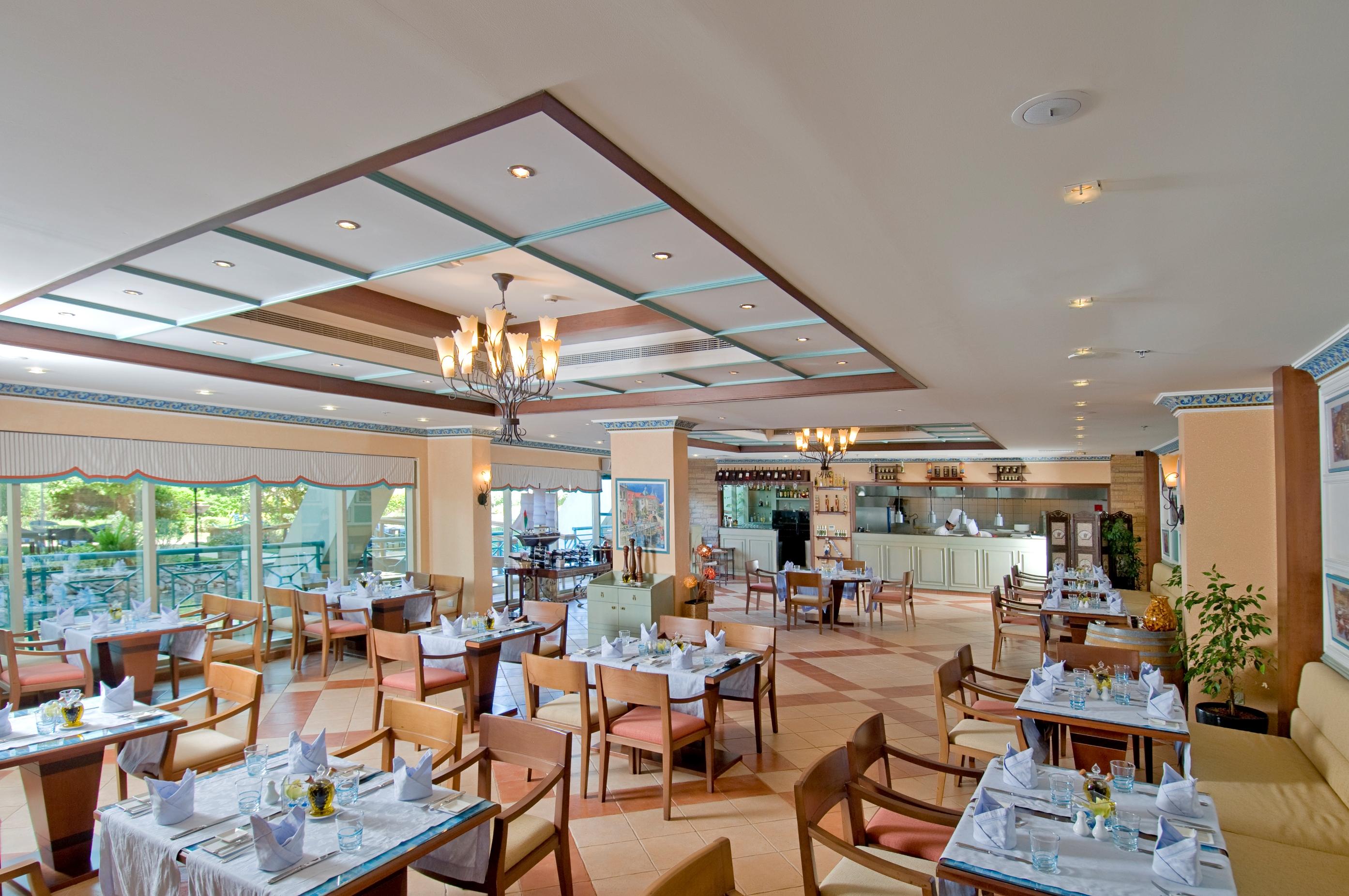 Al Raha Beach Resort & Spa Abu Dhabi Restaurante foto The photo shows the interior of a restaurant. It features a spacious dining area with multiple tables neatly arranged, each set with tableware and cloth napkins. The decor includes a decorative ceiling with lighting fixtures, and large windows that p