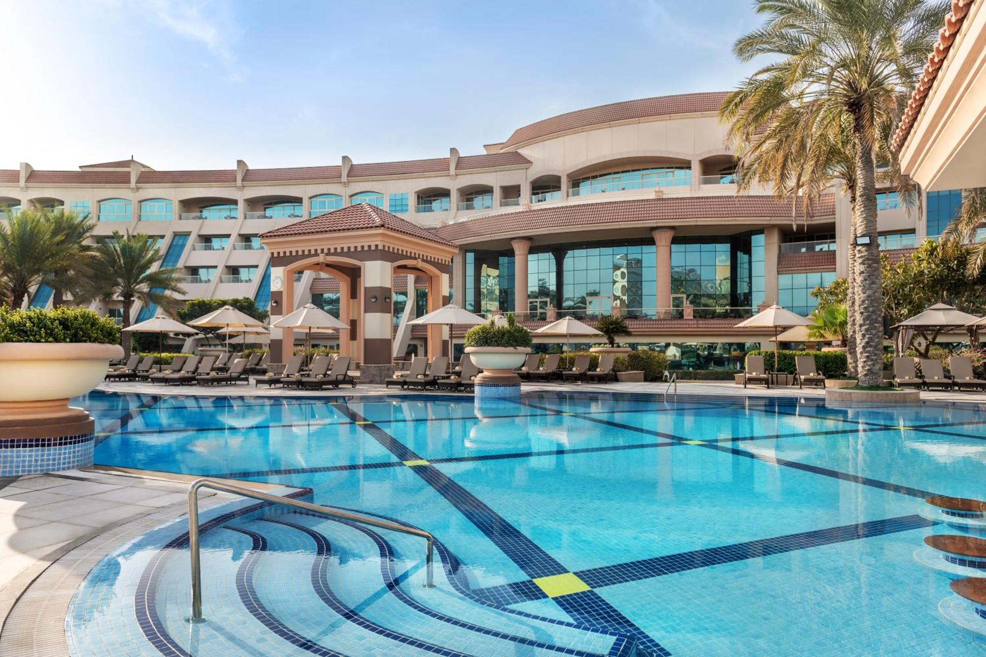 Al Raha Beach Resort & Spa Abu Dhabi Exterior foto The photo shows a luxurious resort with a large swimming pool in the foreground. The pool has a clean, blue surface and features lounge chairs on the surrounding deck. In the background, there is a stylish and modern hotel building with multiple stor