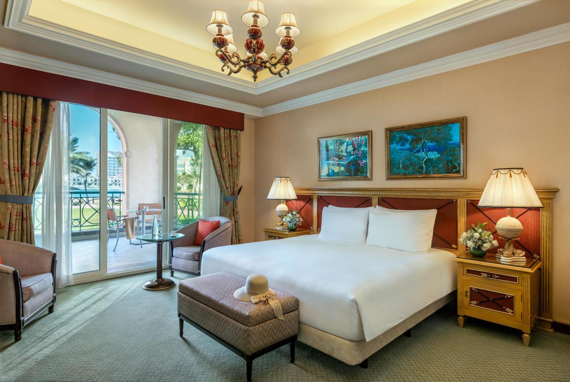 Al Raha Beach Resort & Spa Abu Dhabi Exterior foto The image depicts a well-furnished hotel room. It features a large bed with white linens, flanked by two bedside lamps. Above the bed, there are two pieces of artwork hanging on the walls. To the side, there is a comfortable armchair and a small tabl