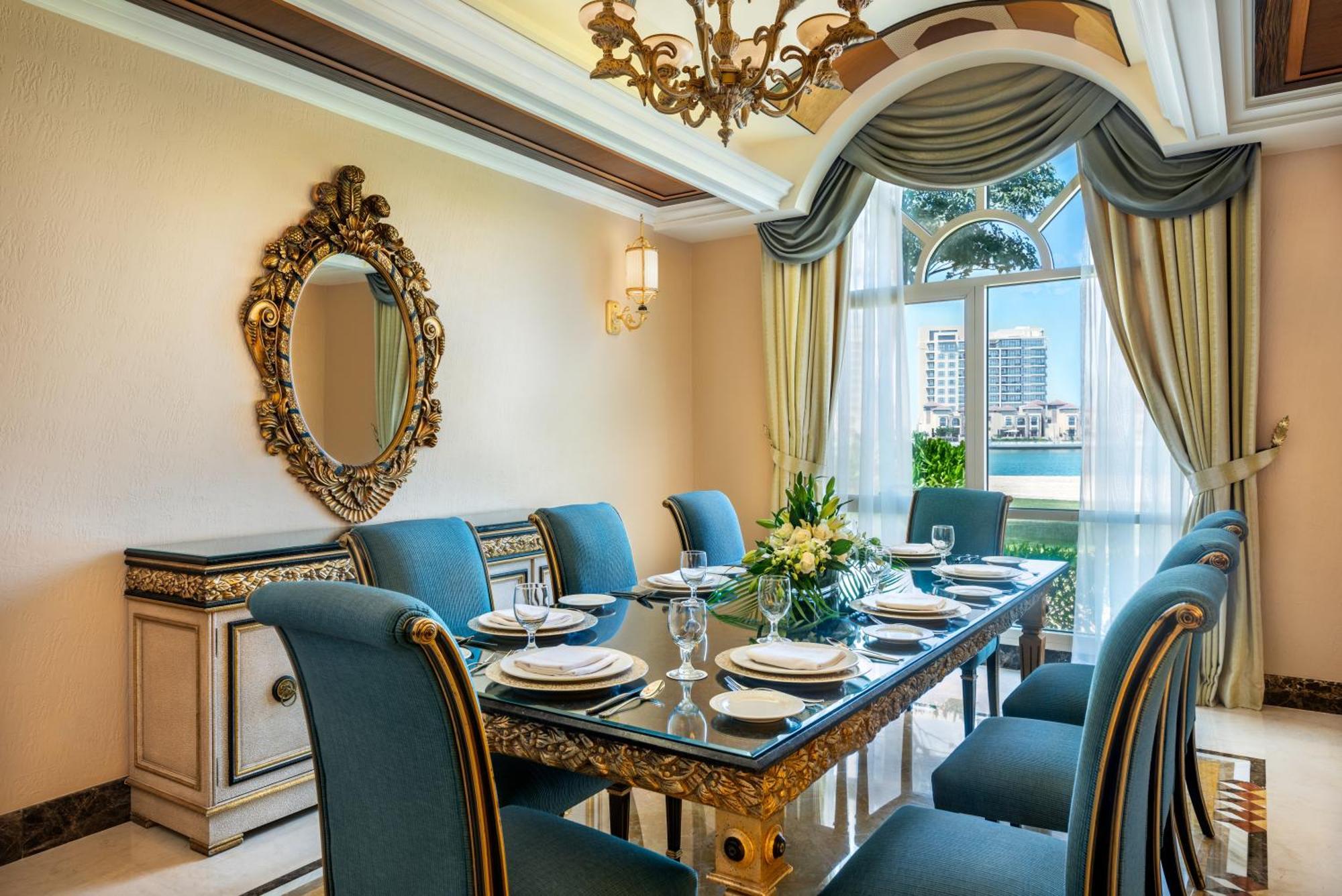 Al Raha Beach Resort & Spa Abu Dhabi Exterior foto The photo features an elegantly decorated dining room. It includes a long, polished table set for a meal with plates, glasses, and decorative items, surrounded by plush blue chairs. The room is adorned with sophisticated details, such as an ornate mi