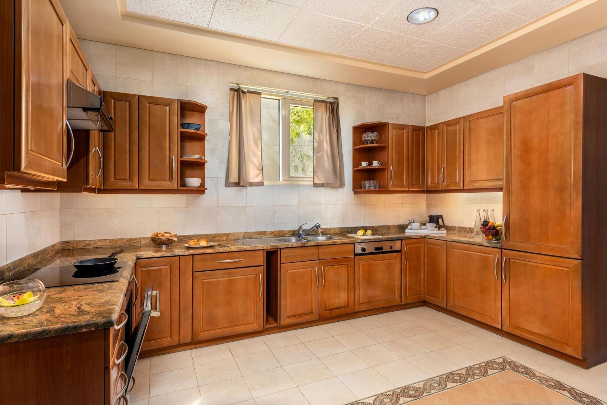Al Raha Beach Resort & Spa Abu Dhabi Exterior foto The photo shows a cozy kitchen featuring wooden cabinets with a rich brown finish, providing a warm and inviting atmosphere. The countertops are made of a light-colored stone, complementing the cabinetry. There is a window above the sink, allowing na