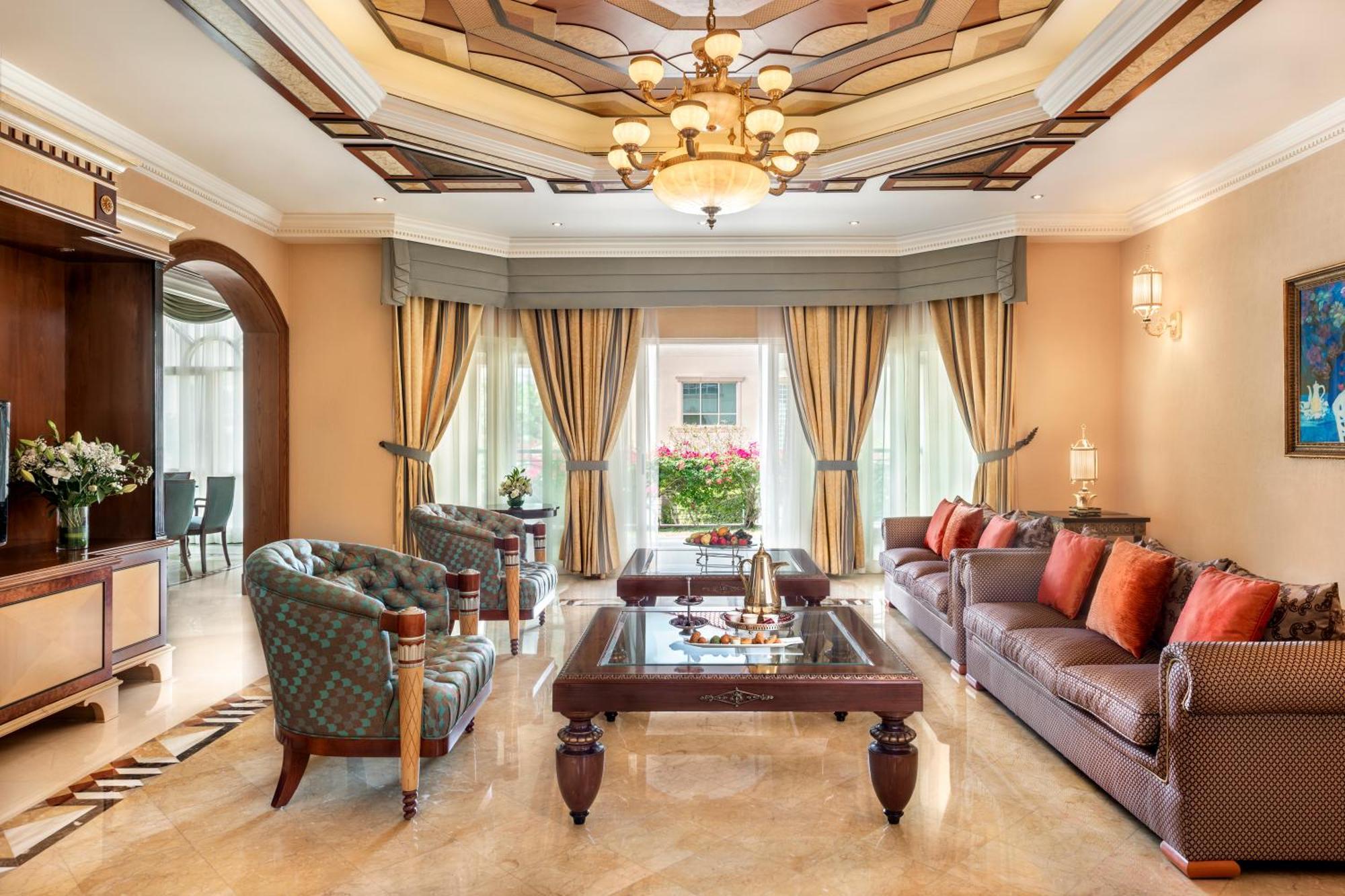 Al Raha Beach Resort & Spa Abu Dhabi Exterior foto The photo shows an elegantly designed living room. It features a high, intricately patterned ceiling with a chandelier hanging in the center. The room is filled with natural light from large windows covered with flowing curtains. 

There are two diff