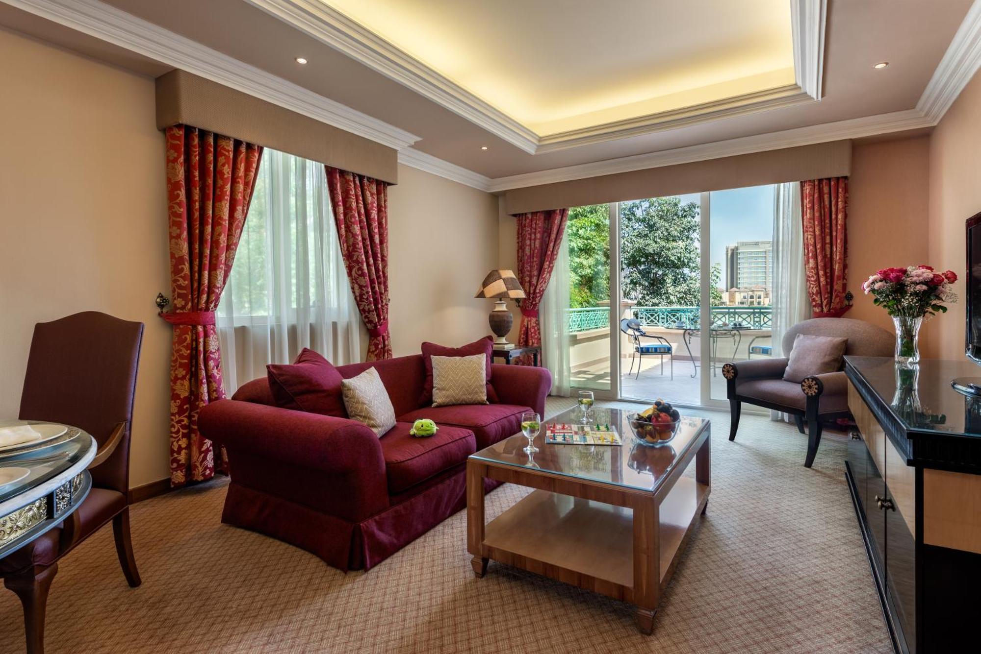 Al Raha Beach Resort & Spa Abu Dhabi Exterior foto The photo shows a well-decorated hotel room or living area. It features a cozy seating arrangement with a deep red couch adorned with cushions, paired with a single chair. There is a glass coffee table in front of the couch, which is set on a plush c
