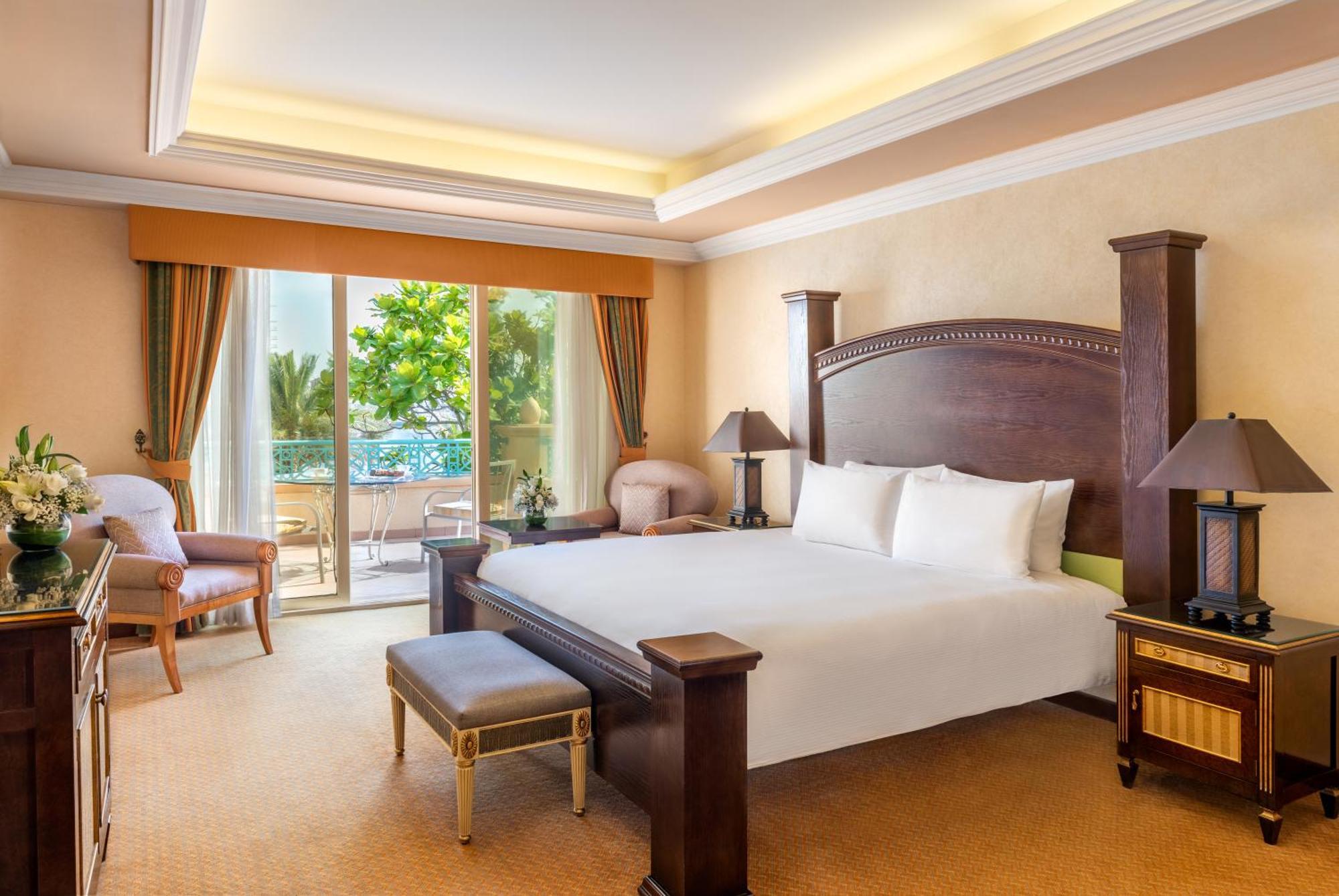 Al Raha Beach Resort & Spa Abu Dhabi Exterior foto The photo shows a well-appointed hotel bedroom. It features a large bed with white bedding, flanked by bedside tables with lamps. The room has light-colored walls and a warm-toned carpet. There is a comfortable seating area with a chair and a small t