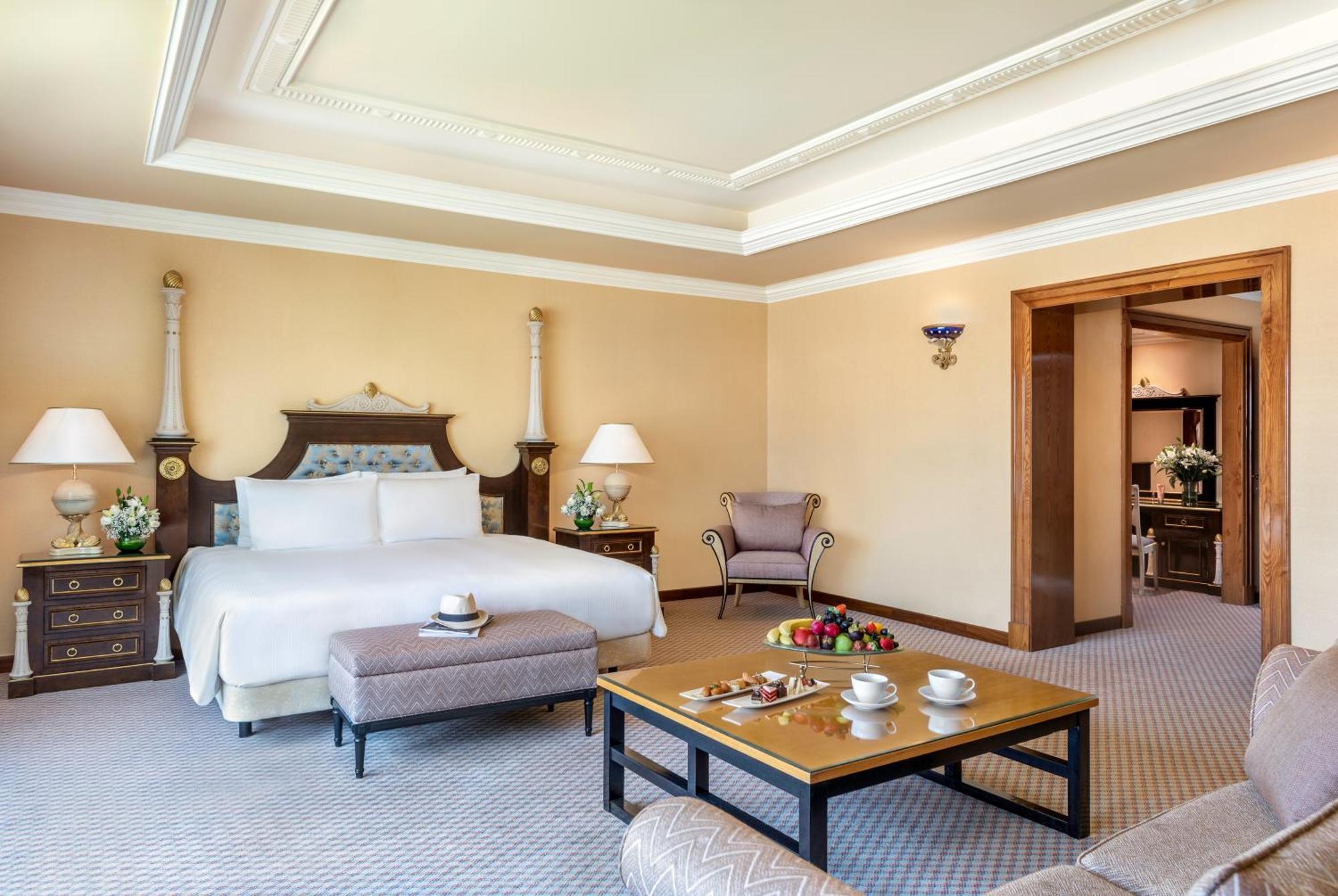 Al Raha Beach Resort & Spa Abu Dhabi Exterior foto The photo shows an elegant hotel room, featuring a large bed with white linens, flanked by stylish bedside tables and lamps. The room has a warm color palette, with light brown walls and a plush carpet. A comfortable armchair is positioned nearby, an