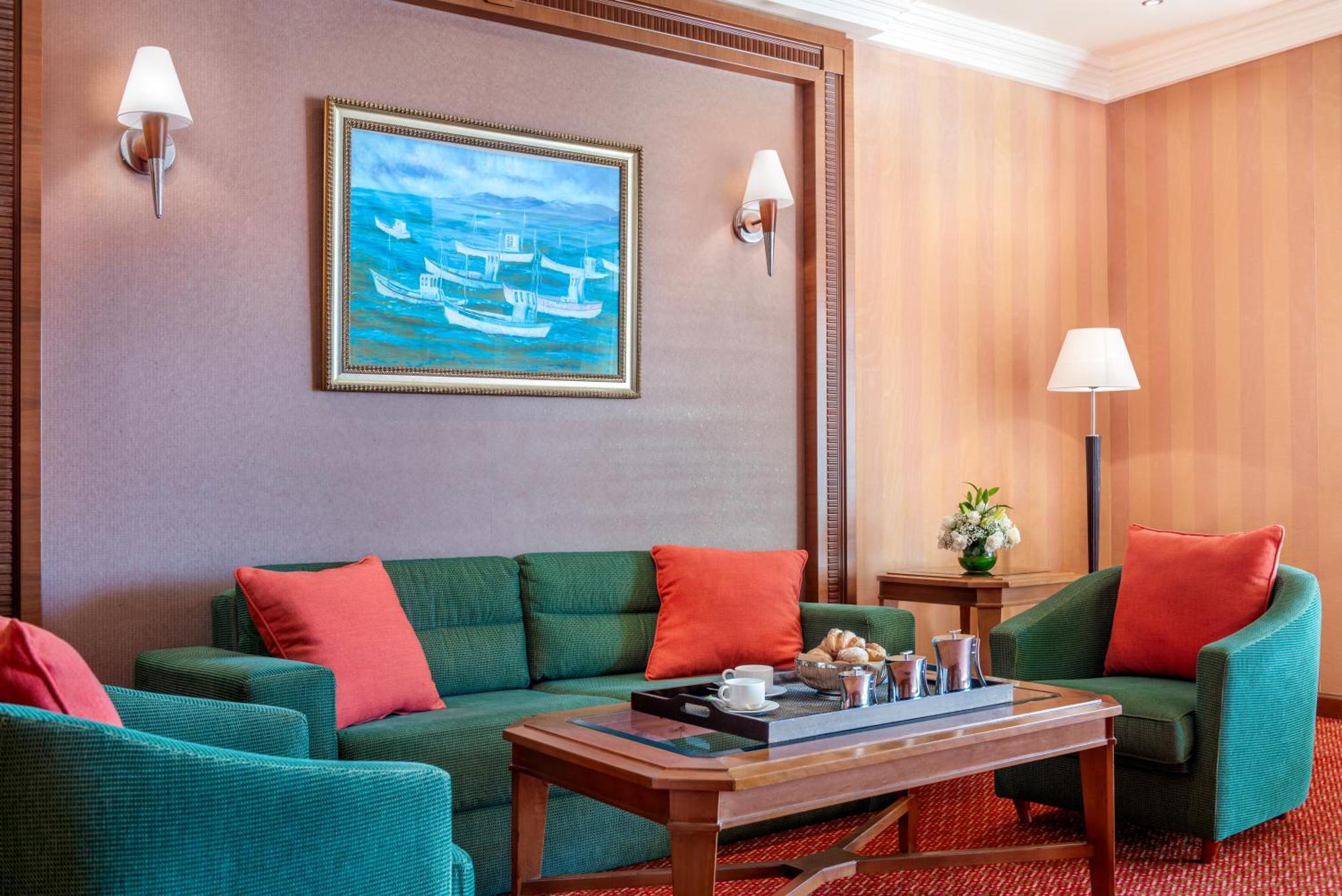 Al Raha Beach Resort & Spa Abu Dhabi Exterior foto The photo displays a cozy and elegantly furnished living area. It features a green sofa adorned with orange cushions and two matching green armchairs. A wooden coffee table sits in the center, which holds a tray with beverages and snacks. The walls a