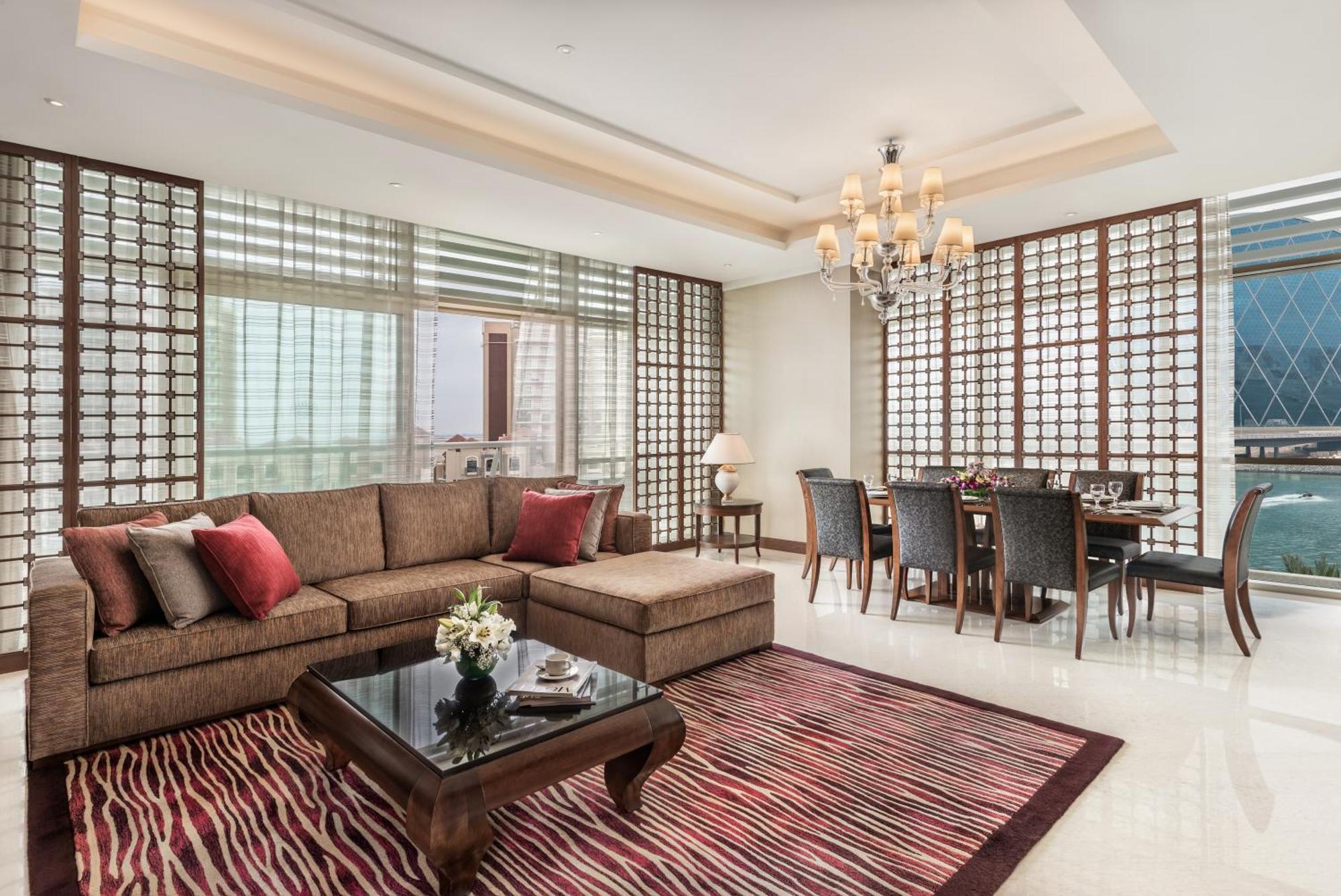 Al Raha Beach Resort & Spa Abu Dhabi Exterior foto The photo shows a stylish and modern living space. On one side, there is a comfortable sectional sofa in a brown upholstery, accented with red and gray cushions. In front of the sofa, there is a glossy black coffee table adorned with a small floral a
