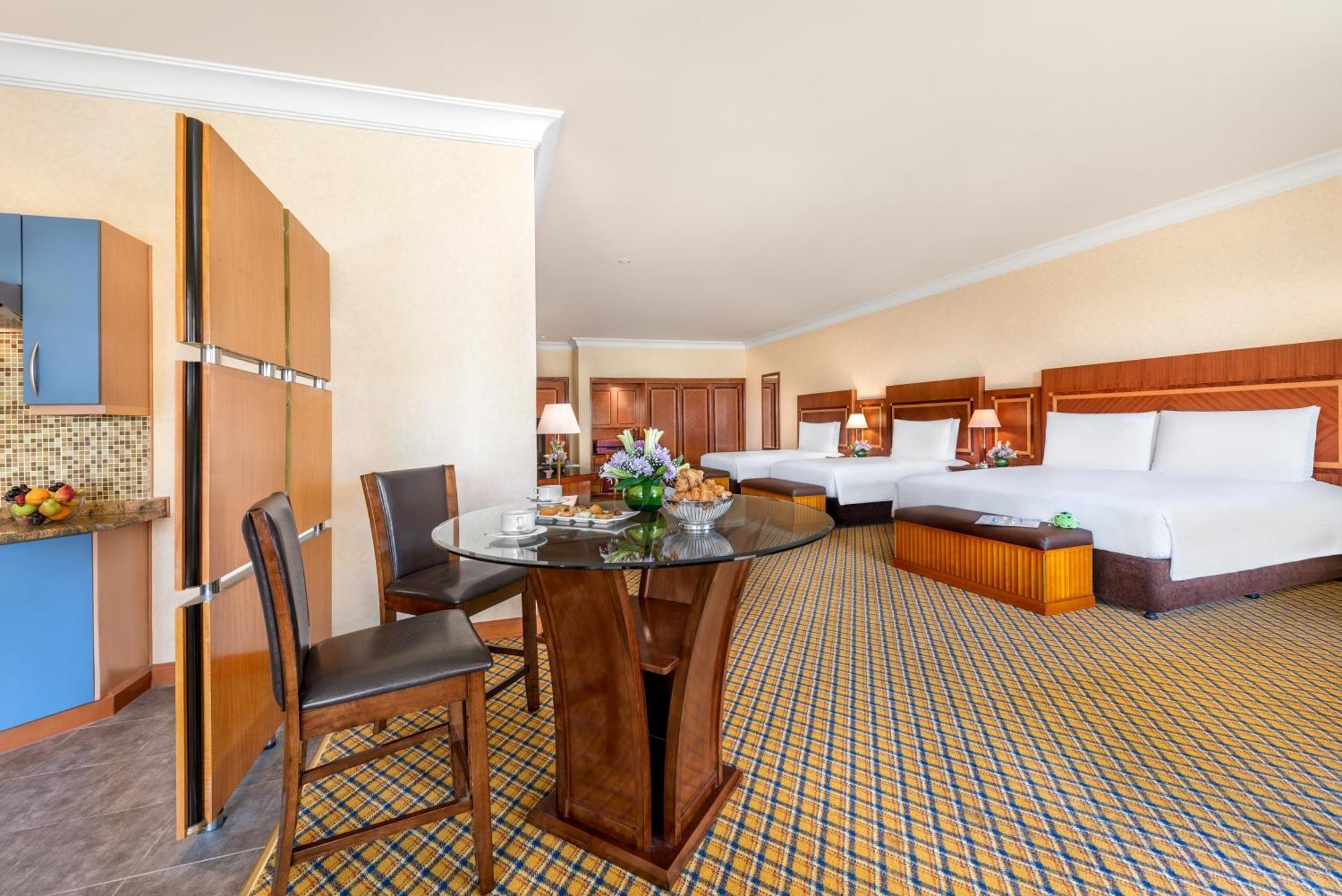 Al Raha Beach Resort & Spa Abu Dhabi Quarto foto The photo displays a spacious hotel room. It features two large beds with white bedding, a circular glass dining table with a decorative floral centerpiece, and a couple of chairs around it. There is a wooden cabinet along one wall, and the room has 