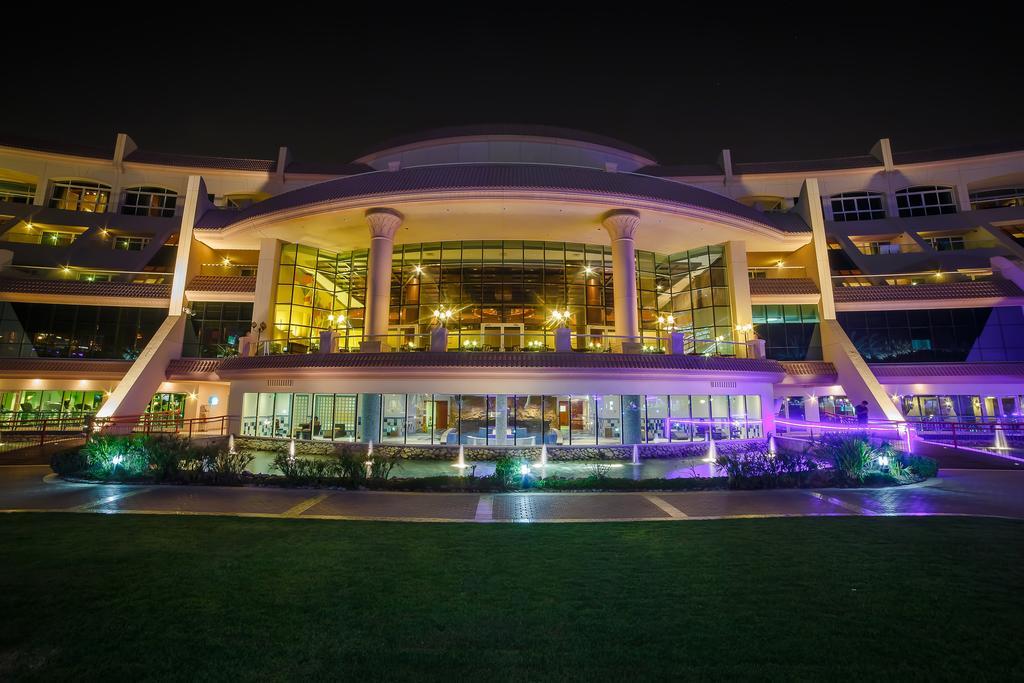 Al Raha Beach Resort & Spa Abu Dhabi Exterior foto The photo shows a modern architectural building illuminated at night. The structure has a large central entrance with multiple glass windows, flanked by symmetrical columns. The exterior features a combination of sleek lines and curves, with lighting
